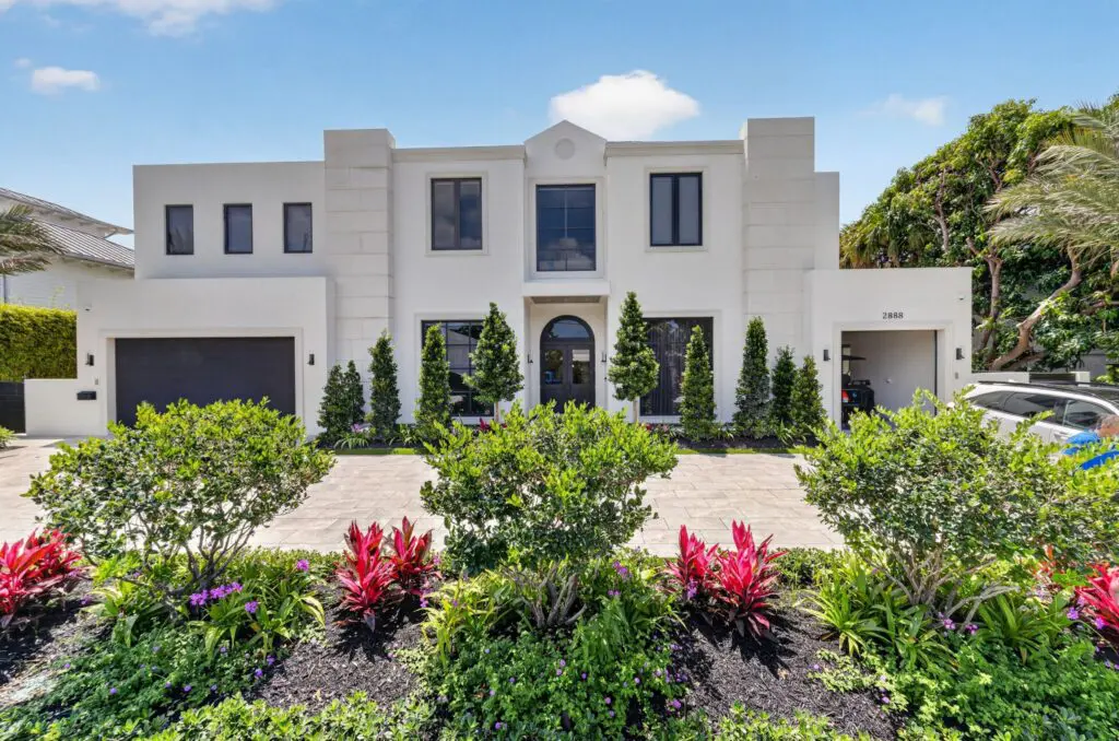Modern white house with symmetrical design, lush landscaping, and pristine paved driveway in Cooper City by Expert Tile & Flooring.